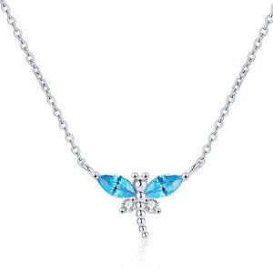 A small blue dragonfly pendant necklace on a gold-plated chain, displayed on a person's neck.