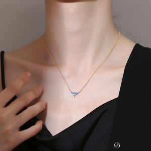 Gold necklace with a blue pendant on a person wearing a black top.