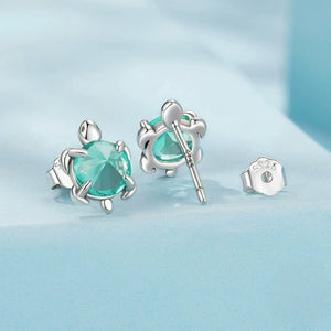 Silver sea turtle-shaped earrings with blue gemstones on a light blue background