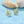 Gold sea turtle-shaped earrings with a light blue center on a light blue background with shells.