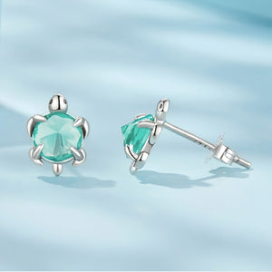Sea turtle-shaped earrings with blue gemstones on a light blue background