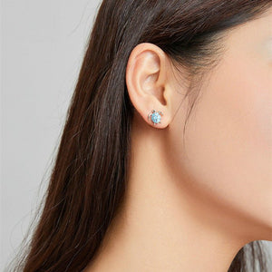 Woman wearing sea turtle-shaped earrings with blue enamel design on a light gray background