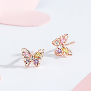 Butterfly-shaped earrings with colorful gemstones on a light pink background