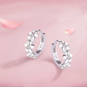 Silver hoop earrings with floral designs on a pink background