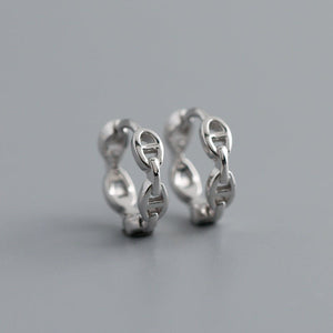 A set of small chain link huggie hoop earrings in silver and gold colors, displayed against a grey background.
