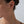 Close-up of a person wearing gold floral earrings against a neutral background