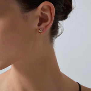Close-up of a person wearing gold floral earrings against a neutral background