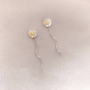 Pair of silver daisy flower earrings on a light beige fabric background