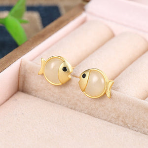 Gold fish-shaped earrings with pearl-like bodies on a soft pink surface.