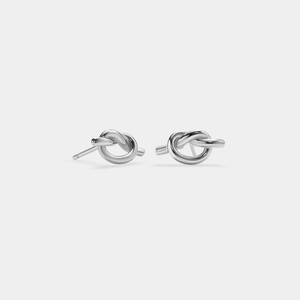 A pair of minimalist heart knot stud earrings in gold color on a white background.