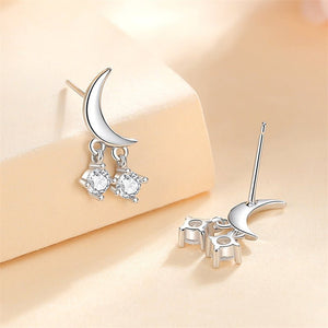 A set of three celestial-themed drop stud earrings, featuring designs resembling moons and stars, in silver and gold colors, embedded with clear stones.