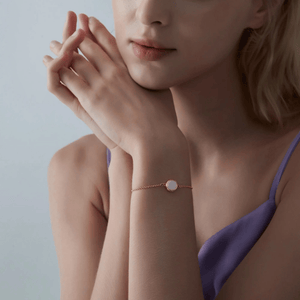 A woman wearing a gold bracelet featuring a small round opal locket with an adjustable chain.
