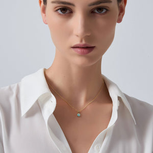 Woman wearing a gold necklace with a small pendant on a plain background