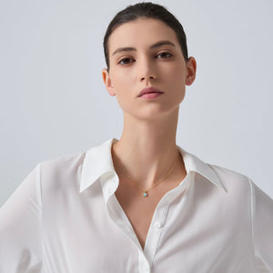 Woman wearing a white shirt and gold necklace against a light gray background