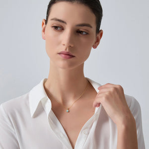 Woman wearing a white shirt and a delicate necklace with a green pendant on a plain background