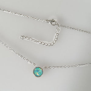 A collection of dainty mini opal charm necklaces laid out on a soft surface, showcasing variations in gold plating colors.