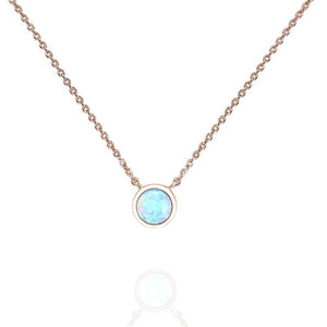 A collection of dainty mini opal charm necklaces laid out on a soft surface, showcasing variations in gold plating colors.