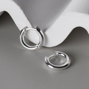 Silver hoop earrings on a gray surface with a white background