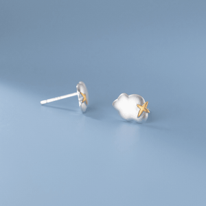 Silver cloud-shaped earrings with a gold star on a light blue background