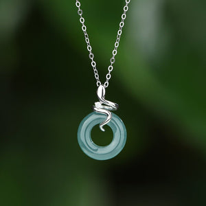 Necklace with a green pendant and silver snake design on a blurred green background
