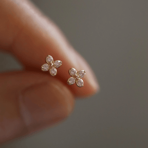Gold flower-shaped earrings held between fingers against a neutral background