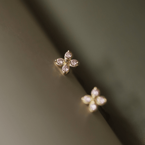 Gold flower-shaped earrings with pink gemstones on a dark background