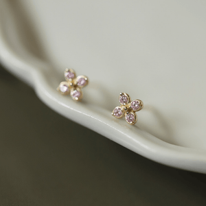 Gold flower-shaped earrings with pink gemstones on a white dish.