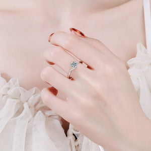 Close-up of a hand wearing a delicate silver ring with a small gemstone on a soft pink background.