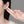 Person wearing a small earring with a hand holding another earring against a gray background