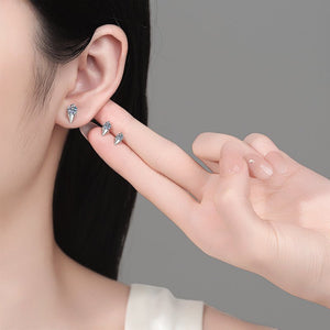 Person wearing a small earring with a hand holding another earring against a gray background