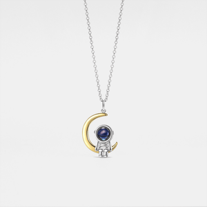 Necklace with a unique pendant featuring a gold crescent moon and silver astronaut design on a light gray background.