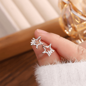 Silver star-shaped earrings held in a hand with a blurred background