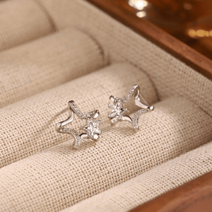 Star-shaped silver earrings with clear stones on a beige fabric surface