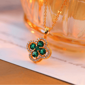Gold necklace with a clover-shaped pendant featuring green stones on a soft surface.