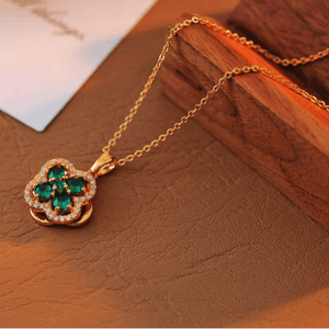 Gold necklace with a clover-shaped pendant featuring green gemstones on a wooden surface.