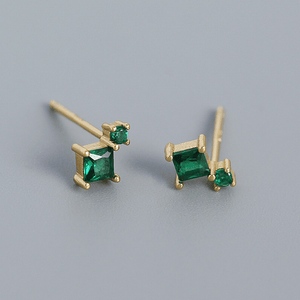 Gold earrings with green gemstones on a gray background