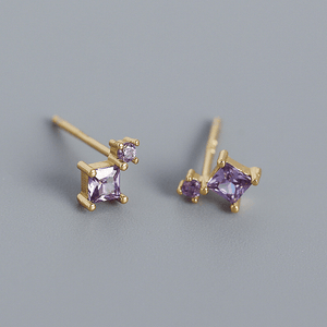 Gold earrings with purple gemstones on a gray background