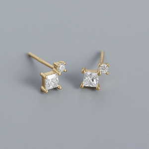 Pair of gold earrings with clear gemstones on a gray background