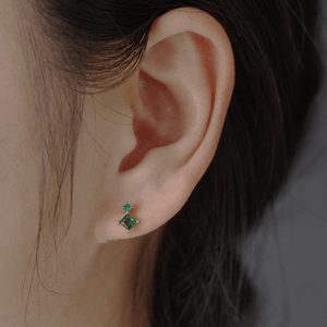 Close-up of an ear wearing a green gemstone earring with a blurred background