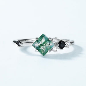 Silver ring with green gemstone and black stones on a light gray background