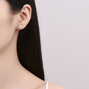 Close-up of a person wearing a silver earring with a clear gemstone on a plain background