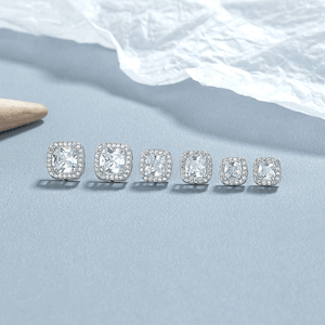 Set of silver stud earrings with clear gemstones on a light blue surface.