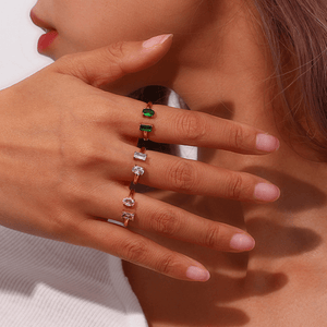 Close-up of a hand wearing a ring with multicolored gemstones on a neutral background