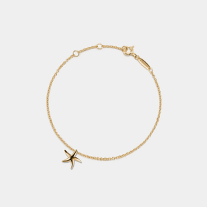 Gold bracelet with a starfish charm on a light gray background