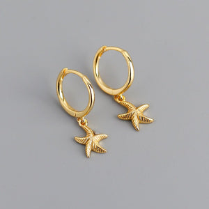 A pair of hoop earrings with starfish charms attached, plated in gold, displayed against a grey background.