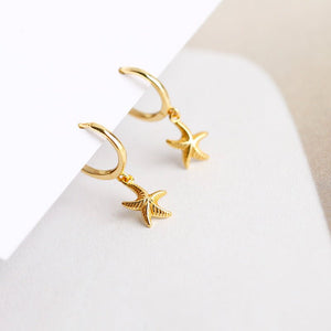 A pair of hoop earrings with starfish charms attached, plated in gold, displayed against a white background.