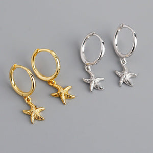 Gold and silver hoop earrings with starfish charms on a gray background