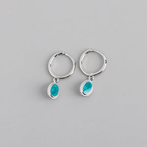 A set of oval drop hoop earrings with a starry night enamel design in blue and green, available in gold and silver finishes.