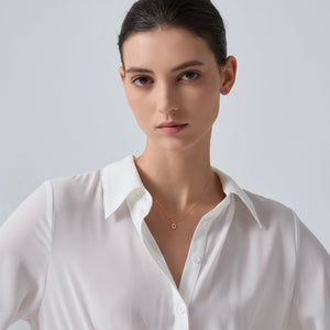 Woman wearing a white shirt and gold sun necklace against a light gray background
