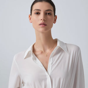 Woman wearing a white shirt and gold sun necklace against a light gray background